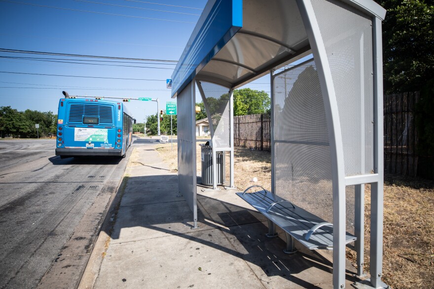 A new bus shelter on the sidewalk, taking up a few feet of space. A blue CapMetro bus is seen pulling away in the background. 