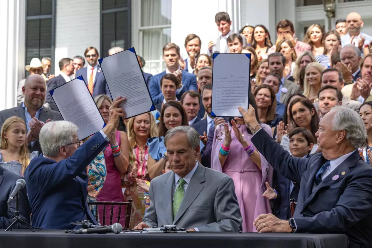 Gov. Greg Abbott signs a set of bills aimed at tightening youth camp safety and strengthening the state's flood preparedness in September 2025. He is flanked by Lt. Gov. Dan Patrick and Texas Rep. Drew Darby, as they raise signed flood relief bills toward families who lost loved ones last July's floods.