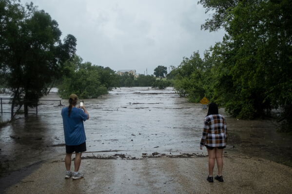 Mike Erulenfeld and Kala Martin watch as the Pedernales River floods near Old Kerr Highway on Thursday, July 16, 2026, in Fredericksburg, Texas. (AP Photo/Joel Angel Juarez)