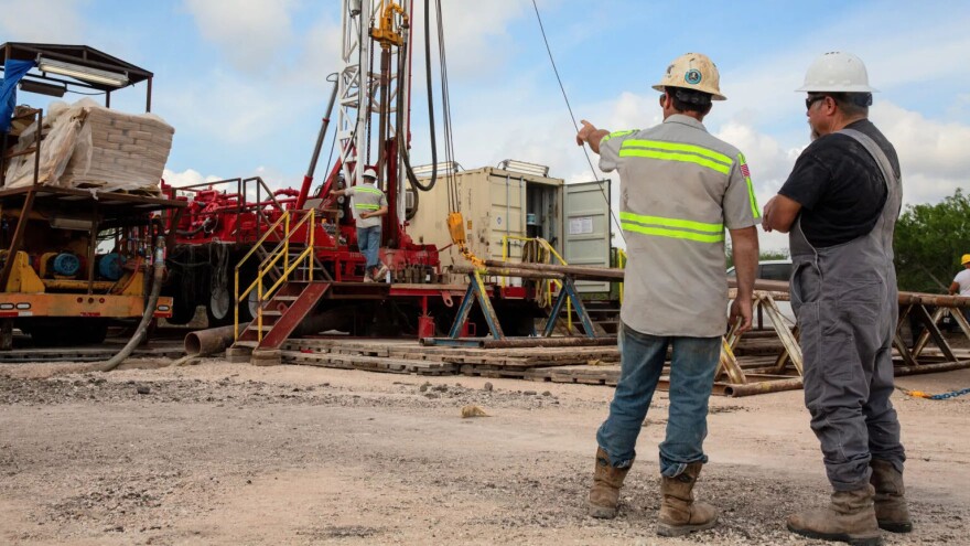 Two workers point and stand next to drilling equipment.