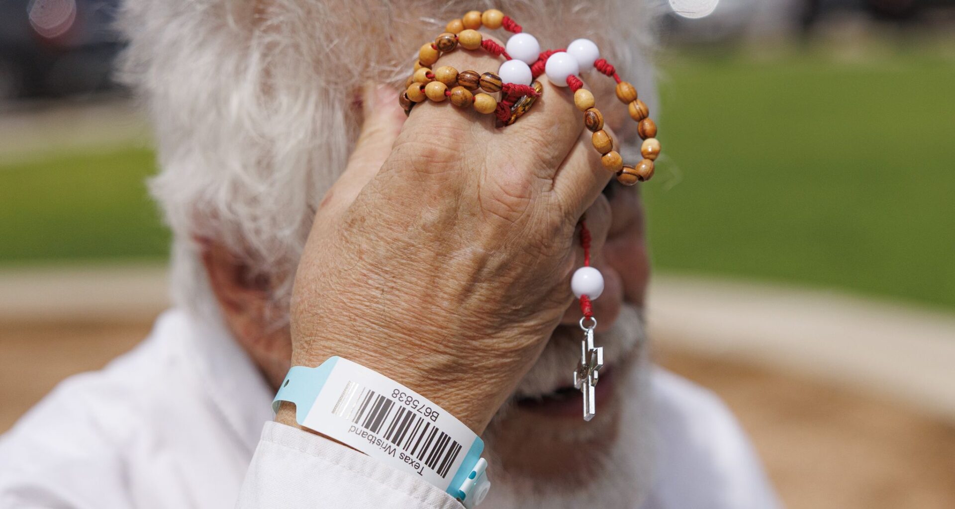 Jim Ollerton wipes sweat from his head while holding one of his handmade rosaries outside the Uvalde County Fairplex in Uvalde on Thursday, July 16, 2026. Ollerton, his wife and their three dogs have been sheltering at the Fairplex since Wednesday with other evacuees from around Uvalde after severe flooding.
