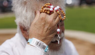 Jim Ollerton wipes sweat from his head while holding one of his handmade rosaries outside the Uvalde County Fairplex in Uvalde on Thursday, July 16, 2026. Ollerton, his wife and their three dogs have been sheltering at the Fairplex since Wednesday with other evacuees from around Uvalde after severe flooding.