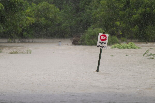 Flood water flows through a restaurant's parking lot on Wednesday, July 15, 2026, in Boerne, Texas. (AP Photo/Darren Abate)