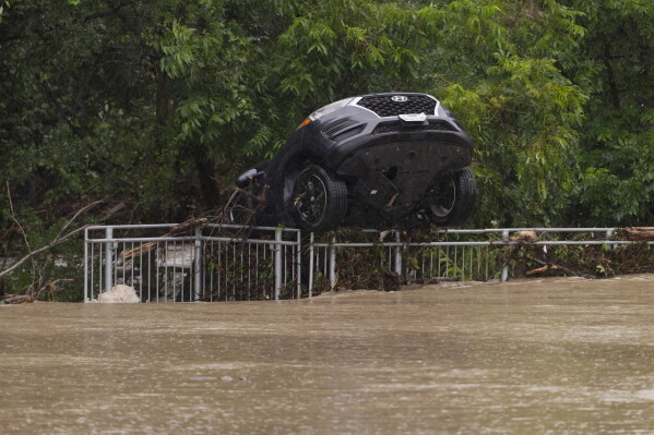 A flood-damaged car hangs from a fence on Wednesday, July 15, 2026, in Boerne, Texas. (AP Photo/Darren Abate)