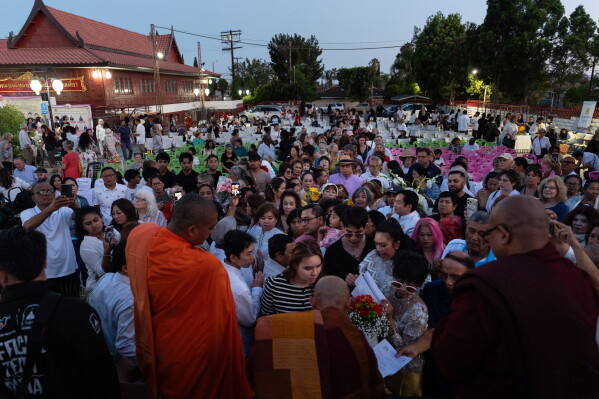 Bhikkhu Pannakara, bottom center, a Buddhist monk who led a Walk for Peace from Fort Worth, Texas, to Washington, D.C., hands out postcards and signs autographs for attendees at Wat Thai of Los Angeles in the North Hollywood section of Los Angeles, Monday, July 13, 2026. (AP Photo/Jae C. Hong)
