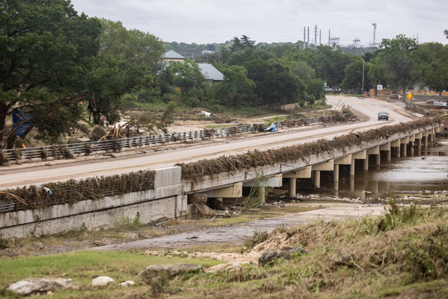 A bridge is covered by flood debris as a car drives over in the background. 
