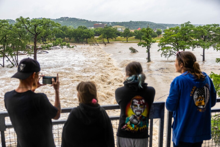 Four people stand and look over a railing at a flooded river.