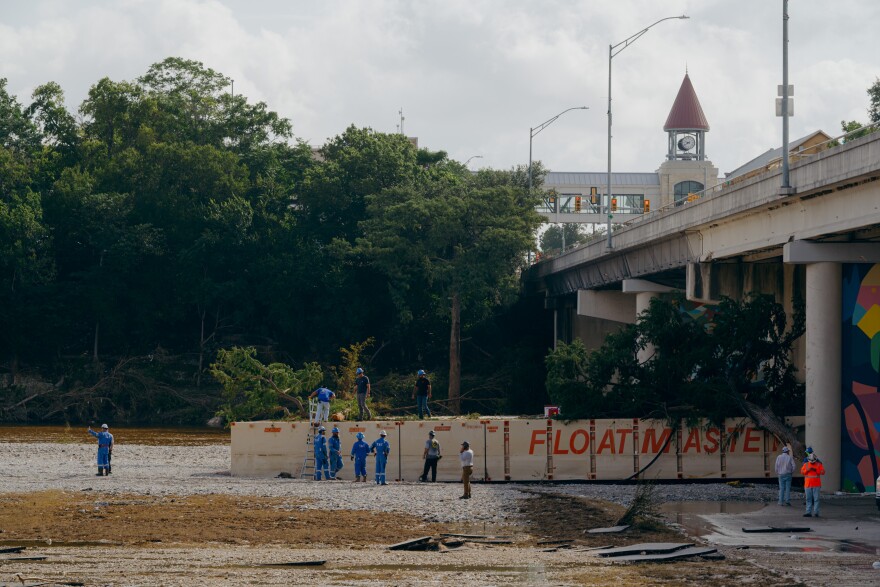 A clean up crew clears trees off a barge stranded under a bridge.