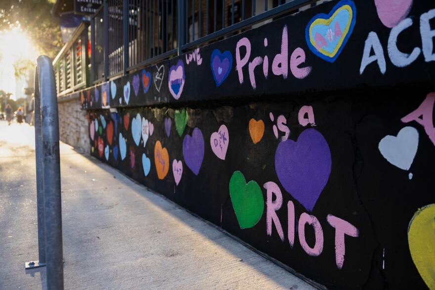 A mural on a wall reads "Pride is a Riot" and has hearts all over it.