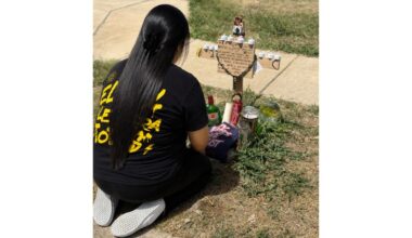 Angelica "Angie" Gonzalez, Janelle Bello's aunt, kneels at the site of the July 8 fatal shooting in front of a cross bearing both Bello and Ulises Ledesma's names.
