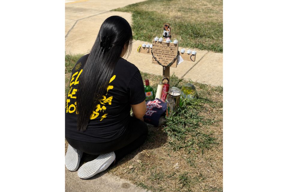 Angelica "Angie" Gonzalez, Janelle Bello's aunt, kneels at the site of the July 8 fatal shooting in front of a cross bearing both Bello and Ulises Ledesma's names.