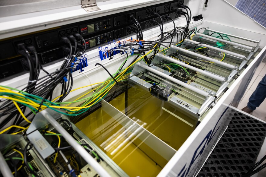 Wires are near and inside a small tank filled with a liquid that is used to cool computer parts.