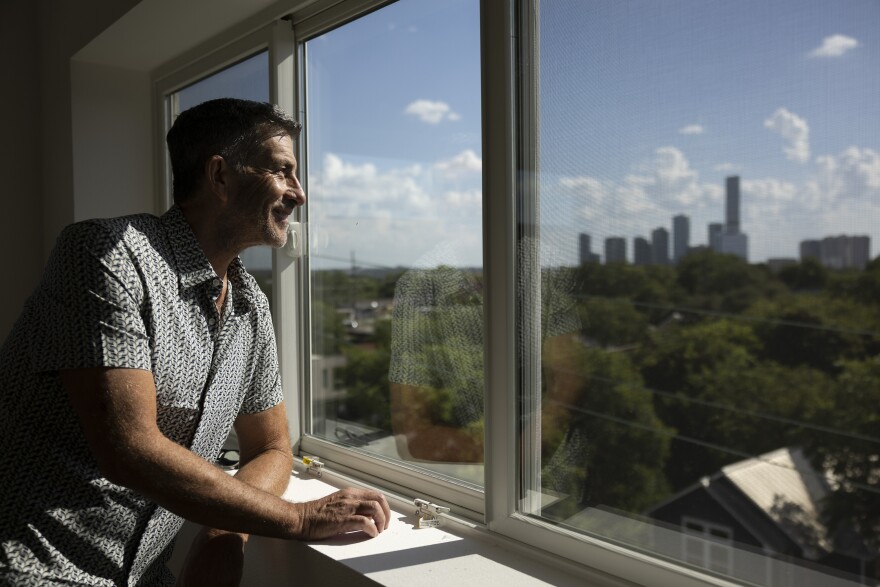 A man looks out a window from a tall building at a skyline in the background.