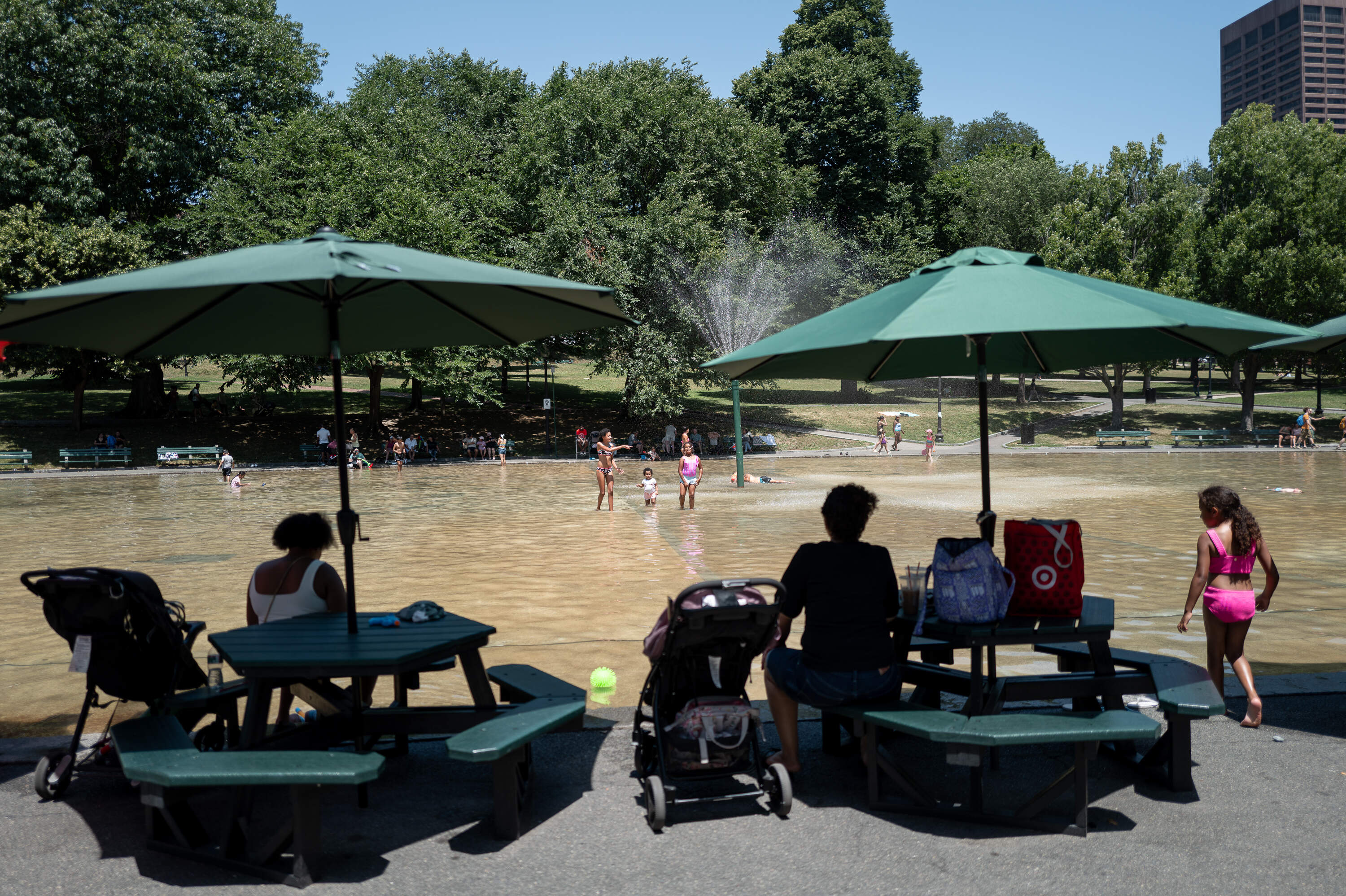Parents watch from nearby tables as their children play in The Boston Common Frog Pond. The spray pool opened for the summer on Friday, July 26, 2026. (Artemisia Luk/WBUR)
