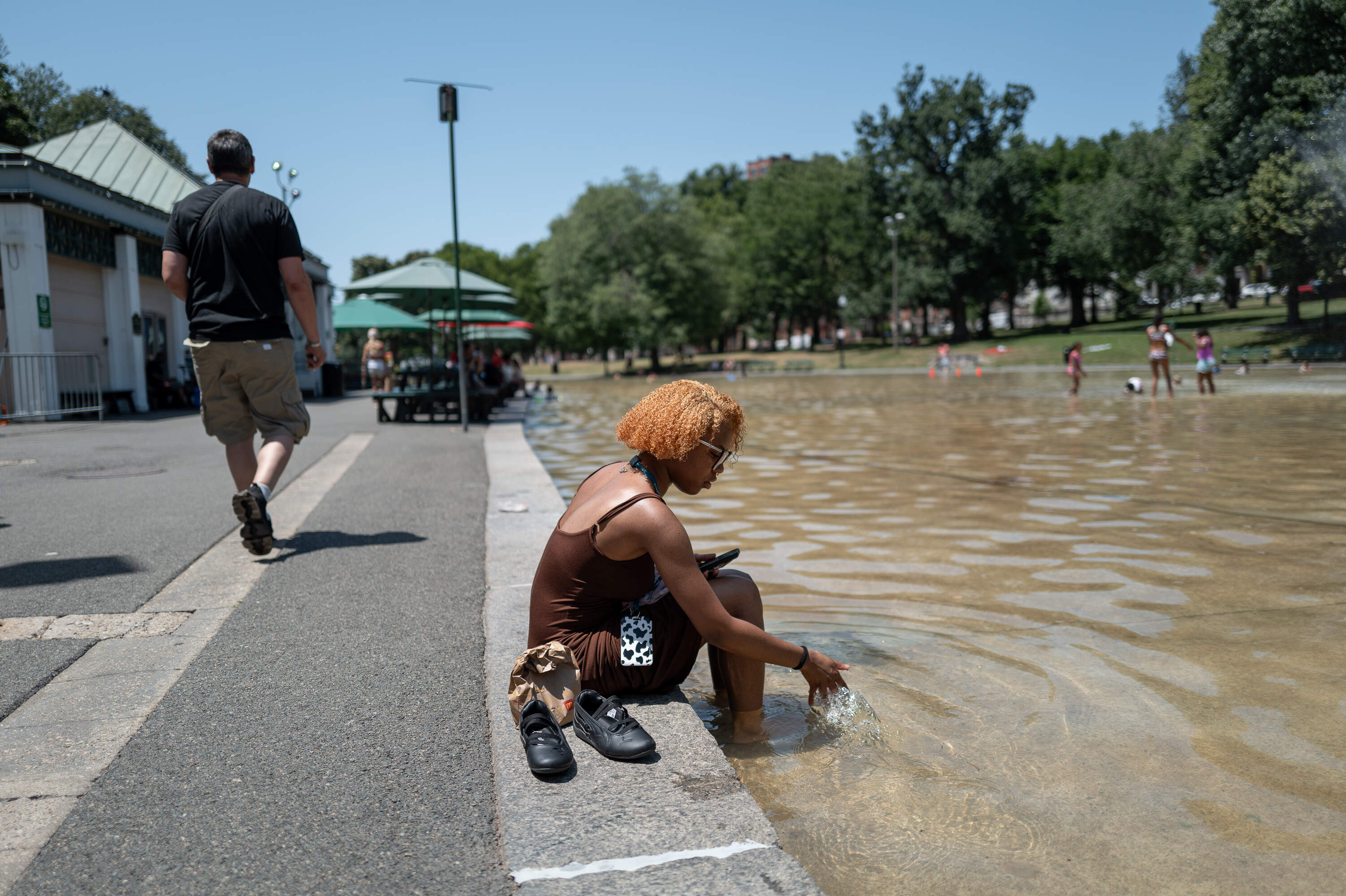 India Wilder dips her feet into The Boston Common Frog Pond during her lunch break. The spray pool opened for the summer on Friday, July 26, 2026. (Artemisia Luk/WBUR)