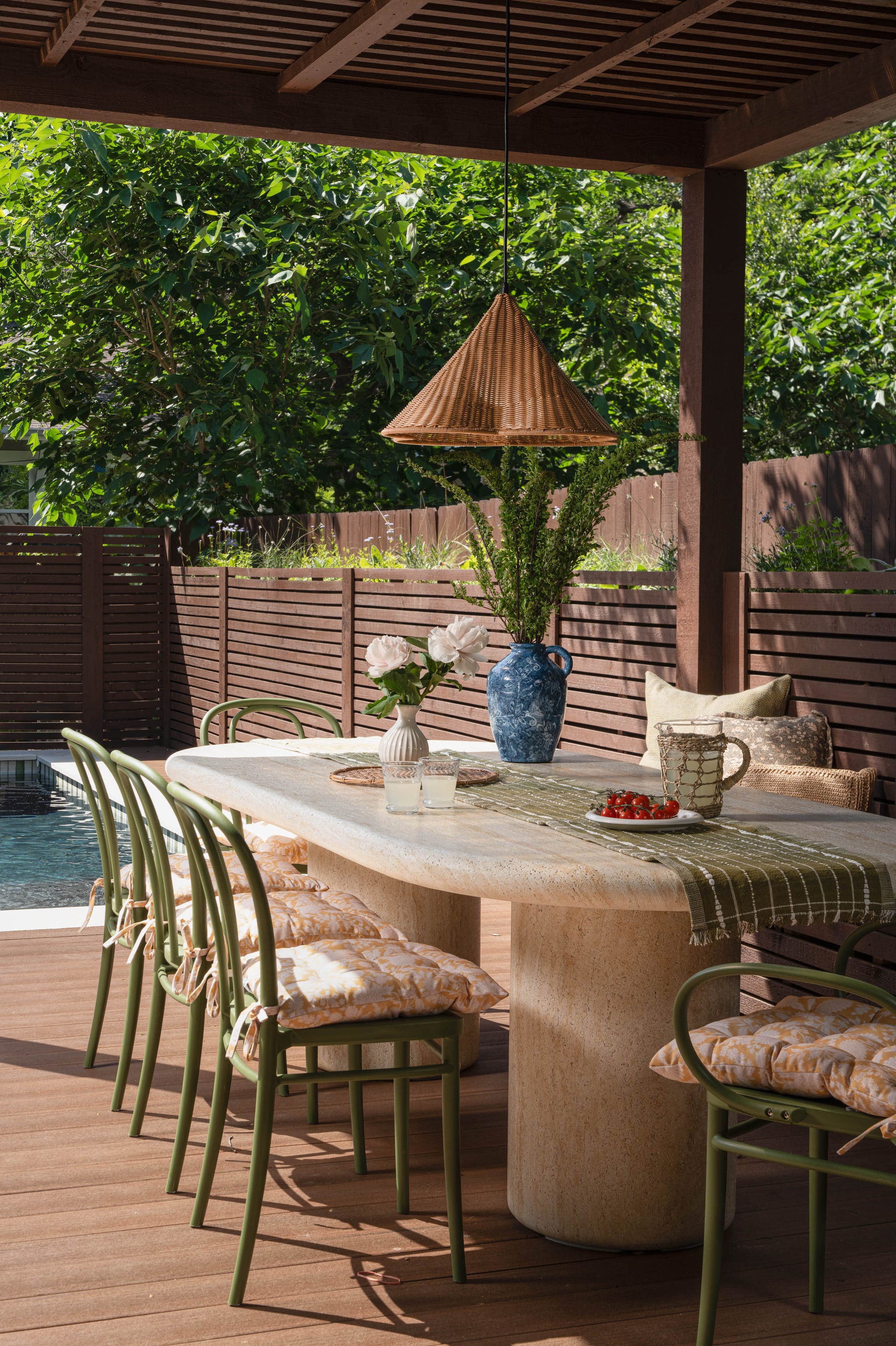Stylish outdoor dining area featuring a long table, decorative plants, and cushioned chairs beside a swimming pool.