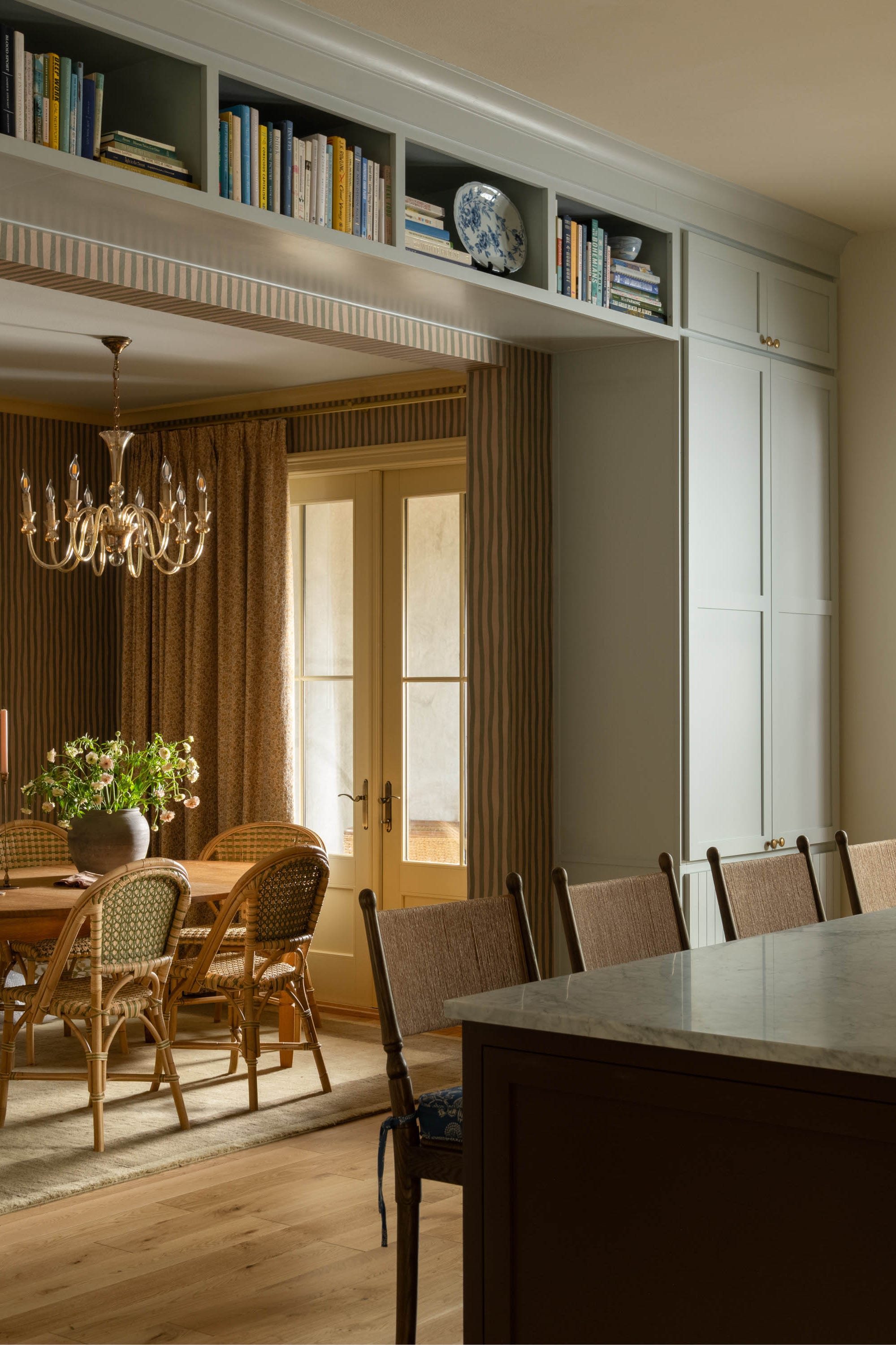 Light-filled kitchen with an island, elegant chandelier, and a cozy dining area featuring a wooden table and rattan chairs. Light-filled kitchen with an island, elegant chandelier, and a cozy dining area featuring a wooden table and rattan chairs.