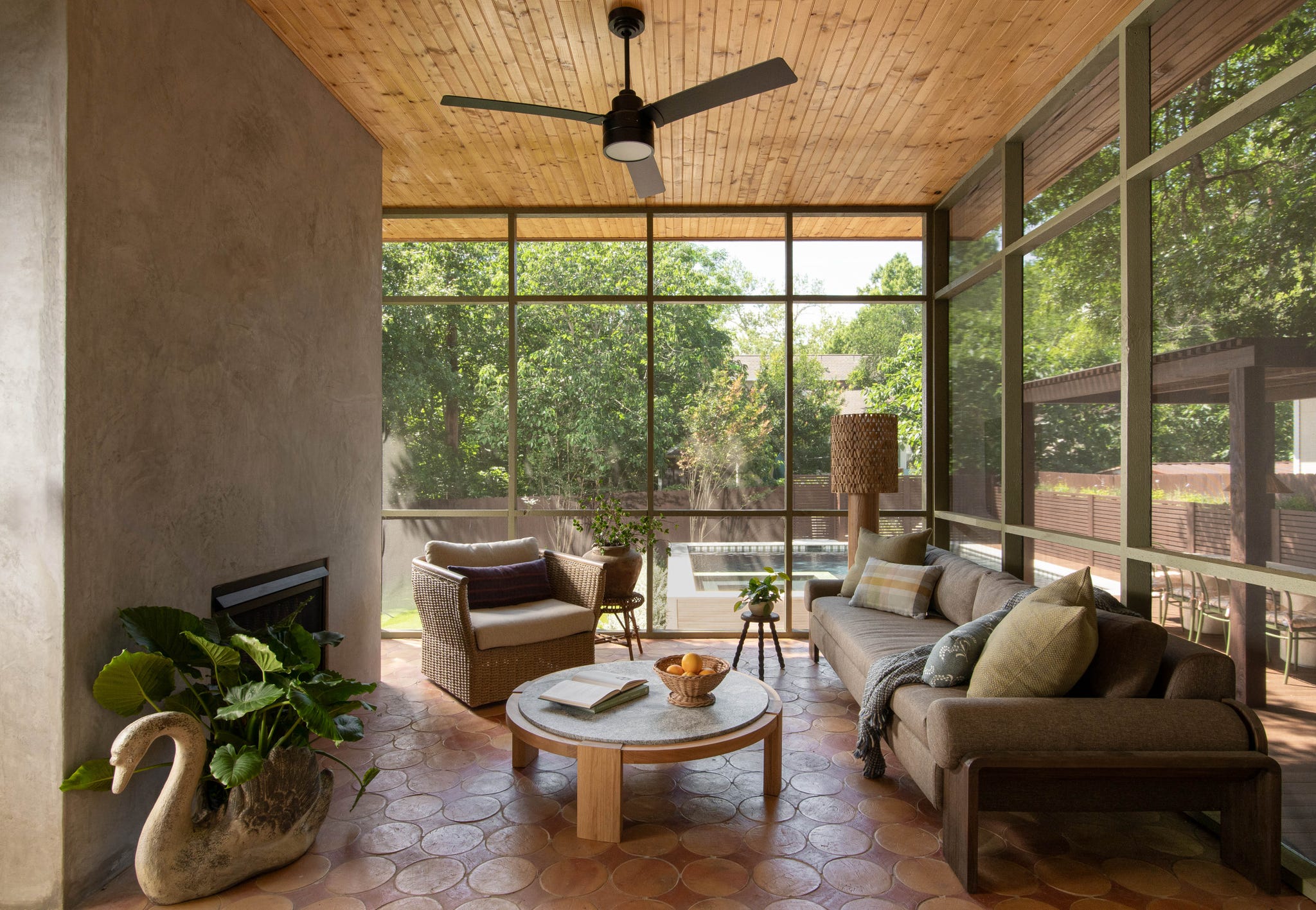 Light-filled sunroom with modern furniture, a coffee table, and views of greenery through large windows.