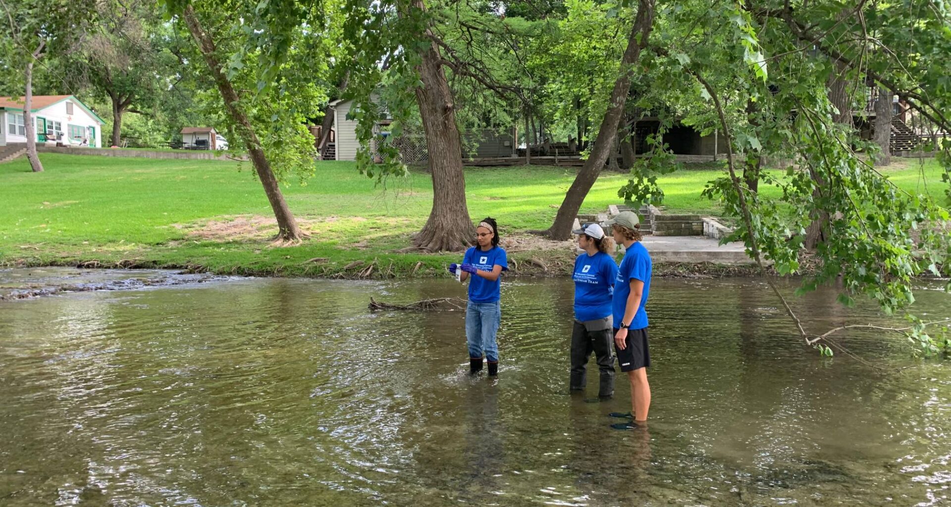 three people in blue shirts standing in shin-deep water