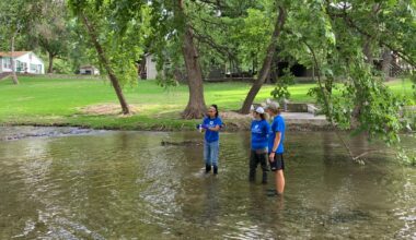 three people in blue shirts standing in shin-deep water
