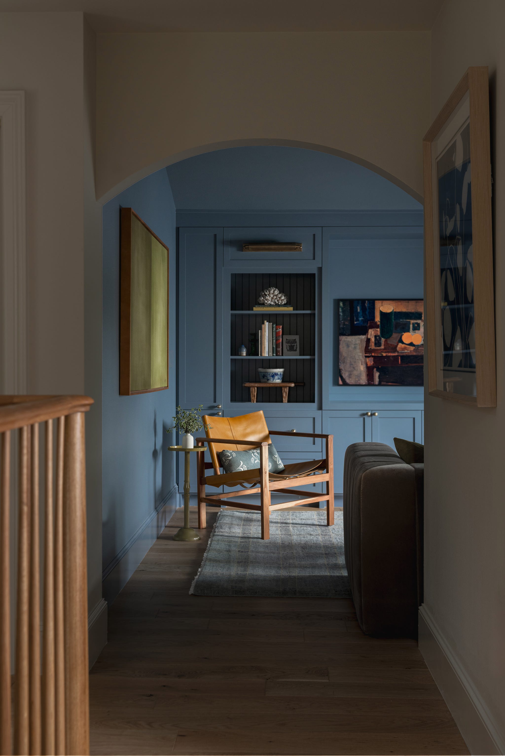 Cozy interior hallway featuring blue walls, a minimalist chair, and decorative artwork on display.