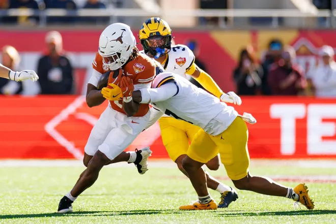 Dec 31, 2025; Orlando, FL, USA; Texas Longhorns wide receiver Ryan Wingo (1) runs with the ball after a catch while Michigan Wolverines defensive back TJ Metcalf (7) tackles during the first half at Camping World Stadium. Mandatory Credit: Matt Pendleton-Imagn Images