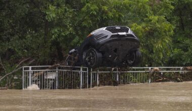A flood-damaged car hangs from a fence on Wednesday, July 15, 2026, in Boerne, Texas. (AP Photo/Darren Abate)