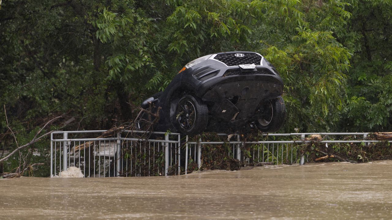 A flood-damaged car hangs from a fence on Wednesday, July 15, 2026, in Boerne, Texas. (AP Photo/Darren Abate)