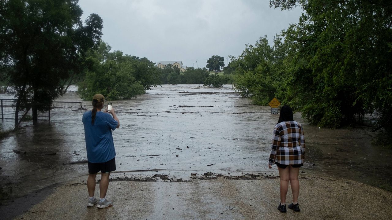 Mike Erulenfeld and Kala Martin watch as the Pedernales River floods near Old Kerr Highway on Thursday, July 16, 2026, in Fredericksburg, Texas. (AP Photo/Joel Angel Juarez)