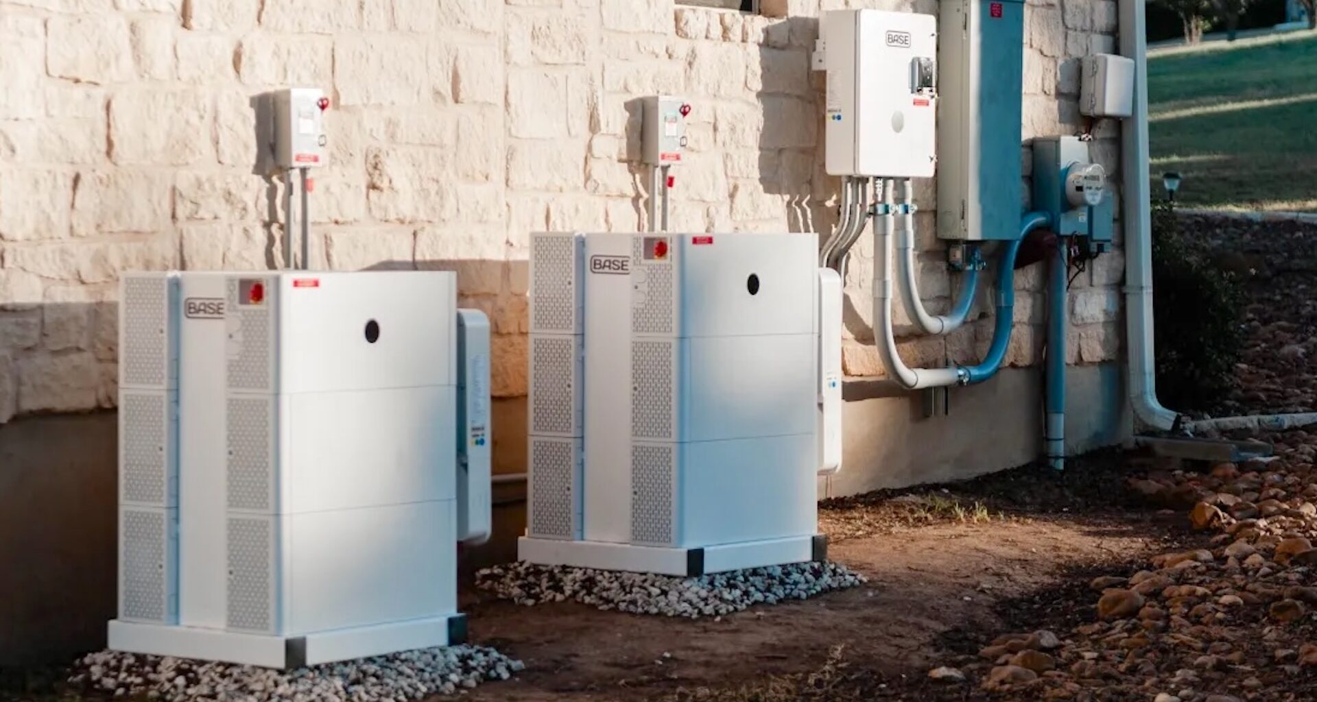 Two white utility boxes installed against a stone wall, featuring electrical components and connected pipes.
