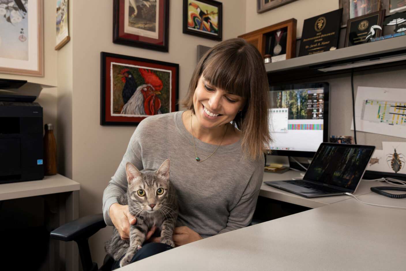 A photo of a woman sitting at a desk with a cat in her lap.