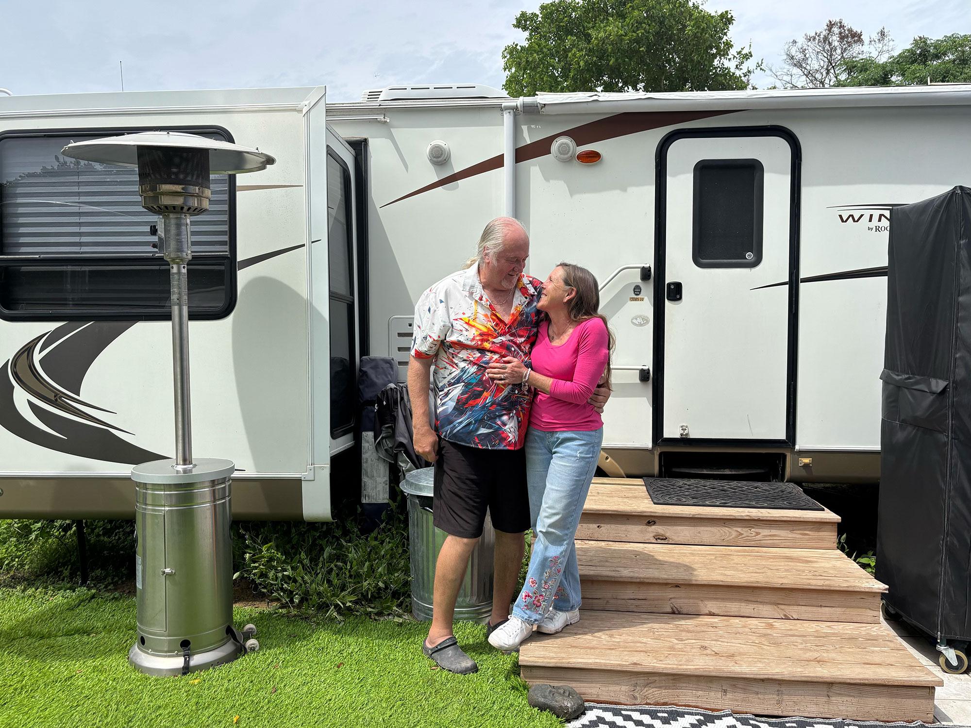 A couple in later middle age stand in front of an RV