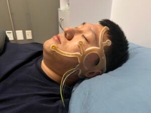 A man lays down in a bed in a lab with his eyes closed. 