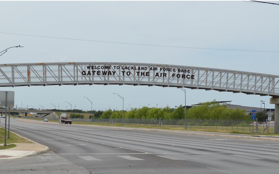 A metal sign with black lettering reading “Welcome to Lackland Air Force Base Gateway to the Air Force” above a multi-lane road.