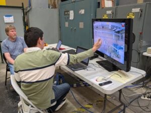 Two researchers sit in a lab watching a demonstration of their power line sensor on a computer. 