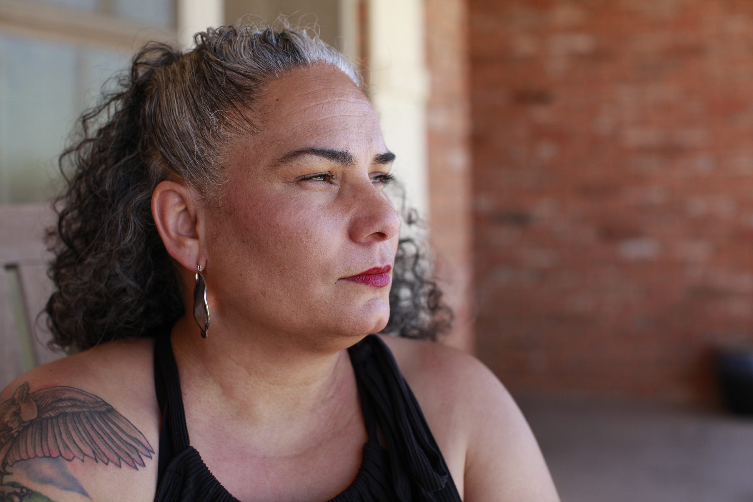 Air Force veteran Omaira Garcia sits on her front porch in Abilene, Texas. She says dust kicked up by construction of OpenAI’s flagship data center next door regularly covers her property. “Coming outside to enjoy time out here has become really difficult for us.” she says.