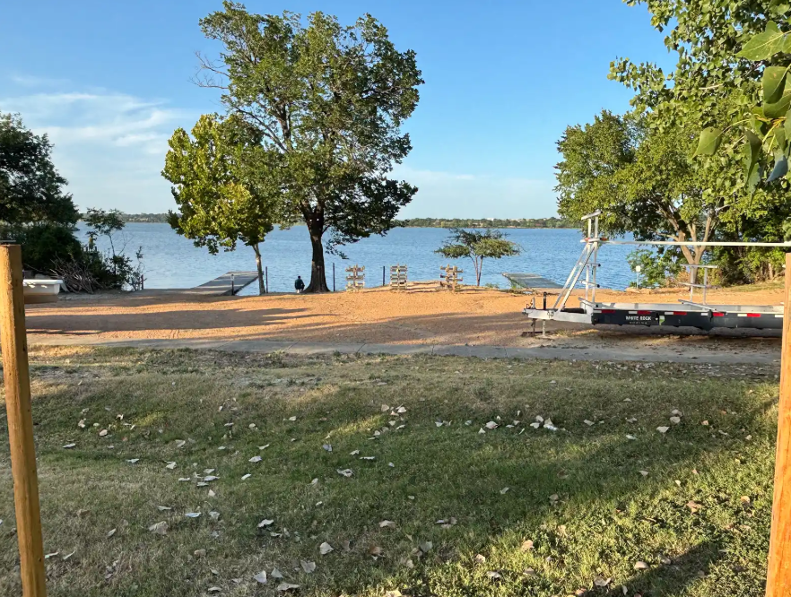 Wooden fence posts with White Rock Rowing's two docks in the background. A man sits between, apparently unaffiliated with WRW.