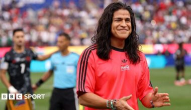 Cristo Fernandez smiling and clapping his hands while wearing a red Adidas t-shirt