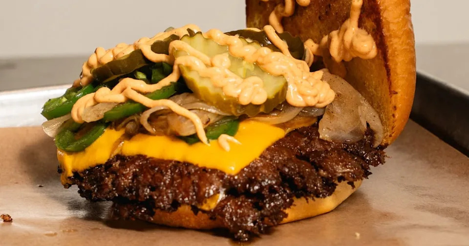 A close up of a smash burger at ZOJAH Burger in San Antonio with cheese, pickles, jalapenos, onions, and special sauce.