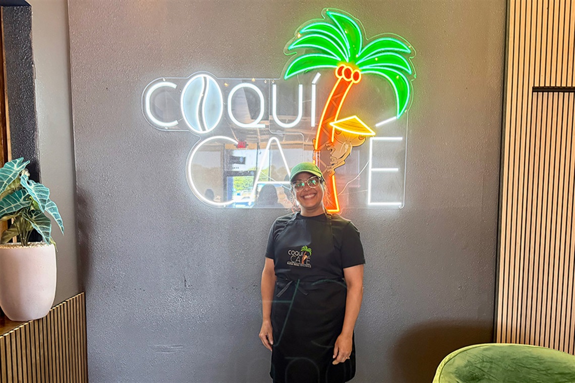 A woman smiling standing in front of a sign that says Coqui Cafe.