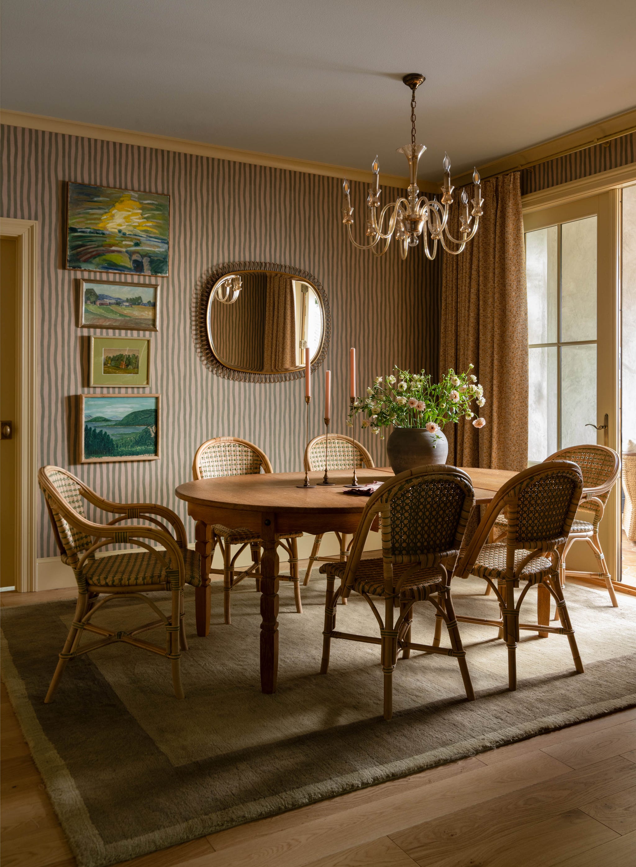 Elegant dining room featuring a round wooden table, wicker chairs, artwork on the wall, and a chandelier overhead.
