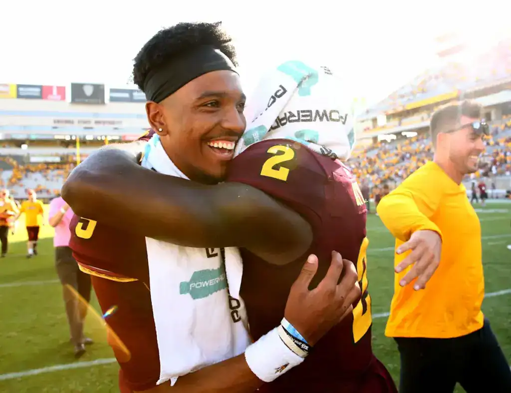 Jayden Daniels smiles while embracing Arizona State teammate Brandon Aiyuk following a Sun Devils football game.