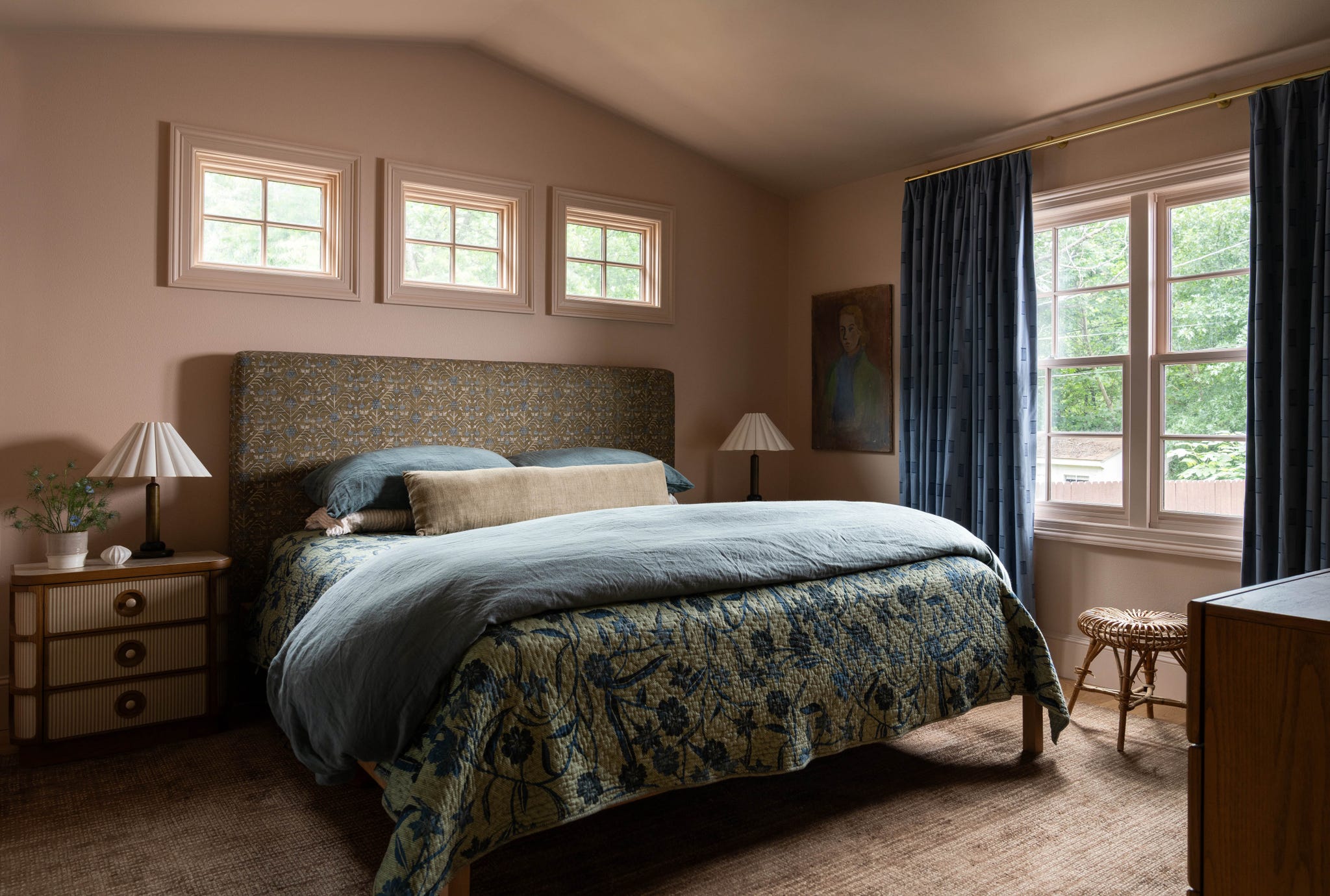 Cozy bedroom featuring a patterned bedspread, framed windows, and decorative lamps, with soft natural light.