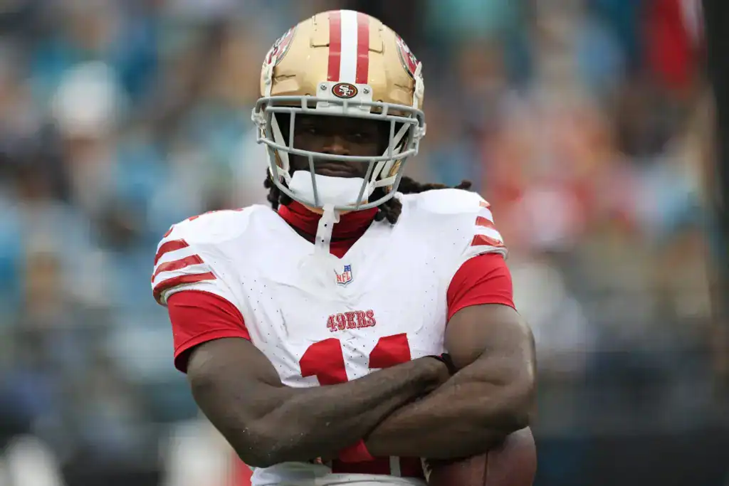 Brandon Aiyuk stands with his arms crossed while wearing the San Francisco 49ers’ white uniform and gold helmet.