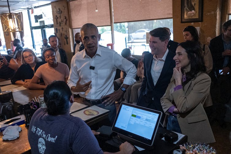 Three people stand at a counter in a taco restaurant