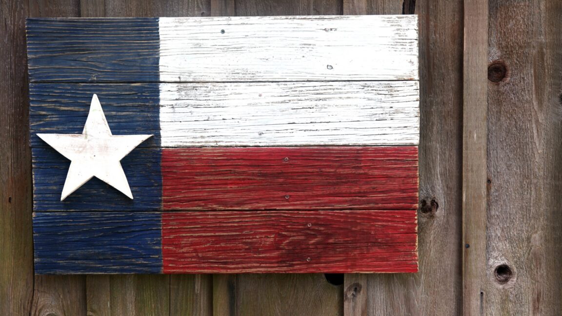 A Texas flag painted on very old boards and hanging on a barn.