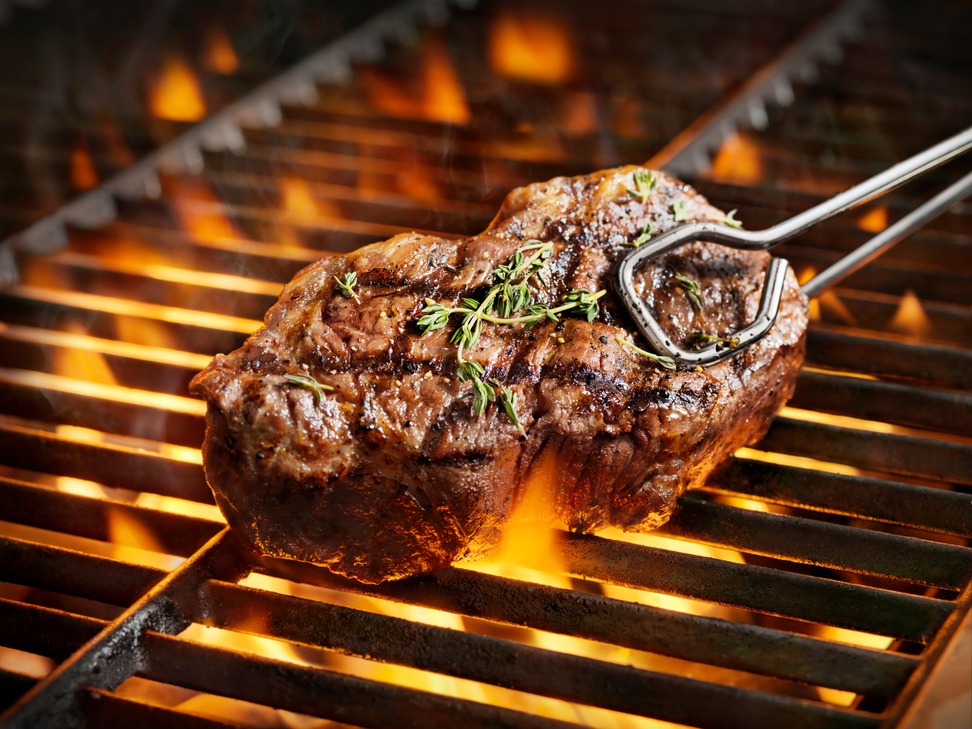 A steak on a grill held by tongs.