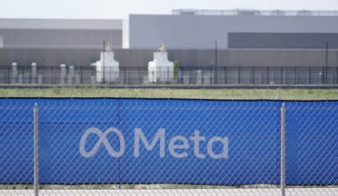 A blue fence with the Meta logo and a background of industrial buildings and green fields.
