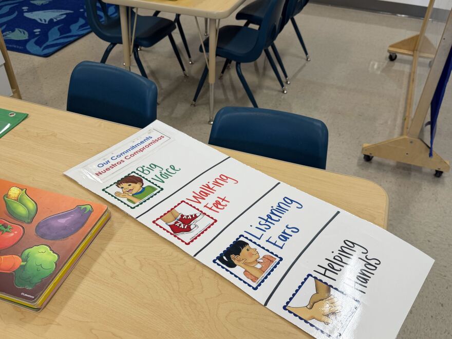 A laminated sheet on a desk has images and the words "Our commitments" at the top and "big voice," "walking feet," "listening ears" and "helping hands" below.