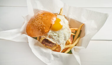 Frita Batidos chorizo burger topped with a fried egg and crispy shoestring fries on a toasted bun, served in a paper-lined basket.